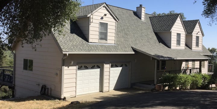 A two-story house with a garage under blue sky, surrounded by trees.