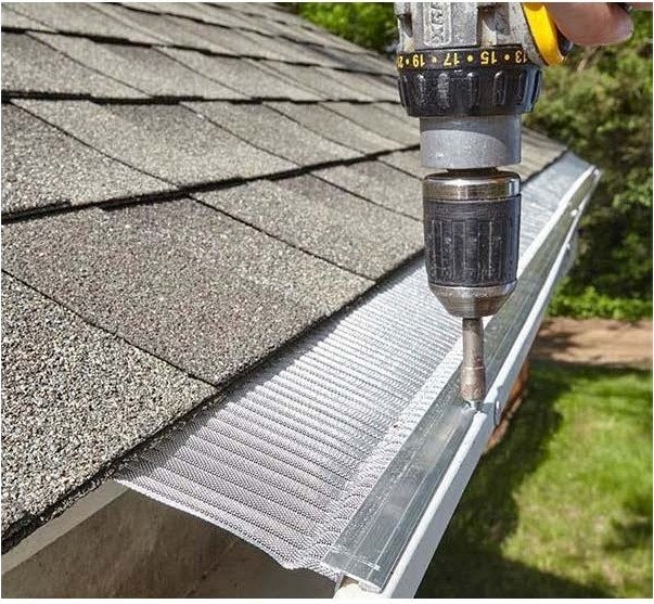 A drill secures a mesh guard to a rooftop gutter.