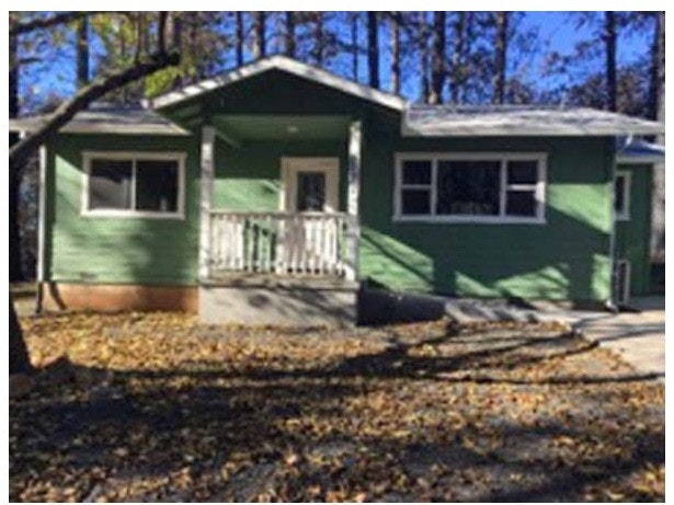 A small, green house with a front porch and fallen leaves on the ground.
