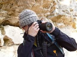Person in a beanie taking a photo with a DSLR camera outdoors near a rocky surface.