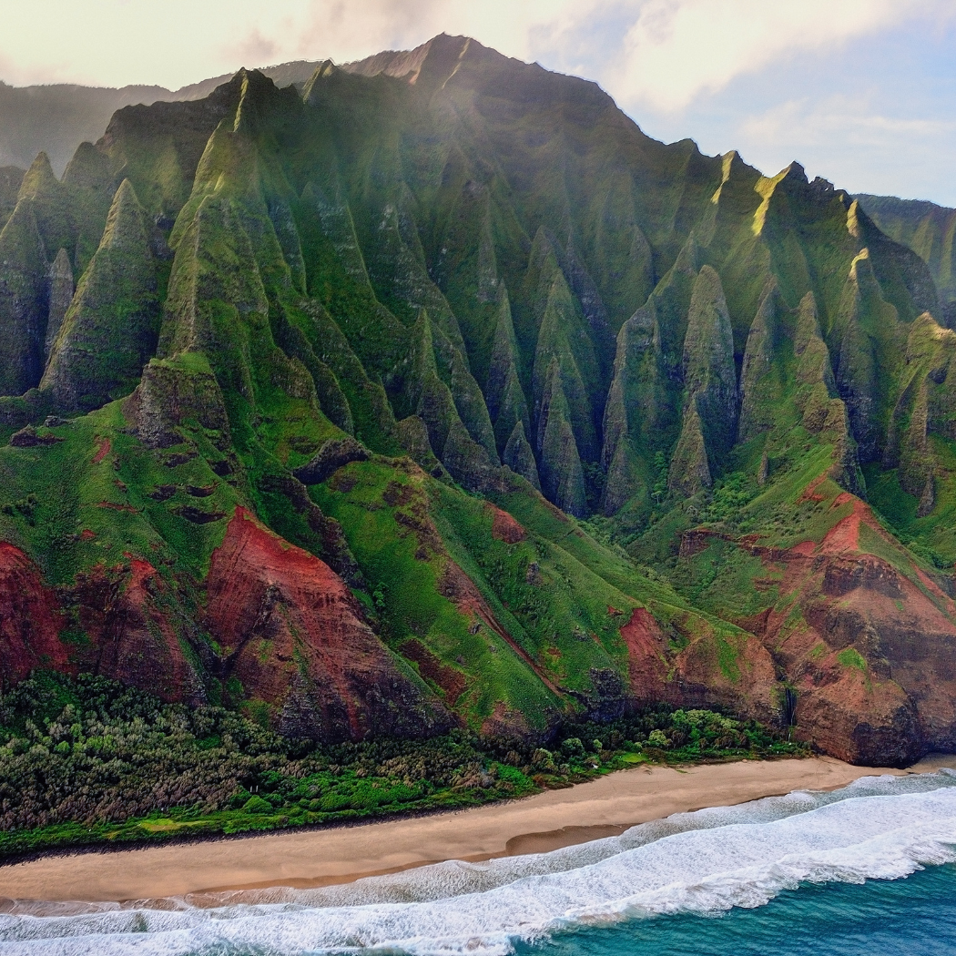 Lush green mountains with sharp ridges and a beach with waves crashing upon the shore.