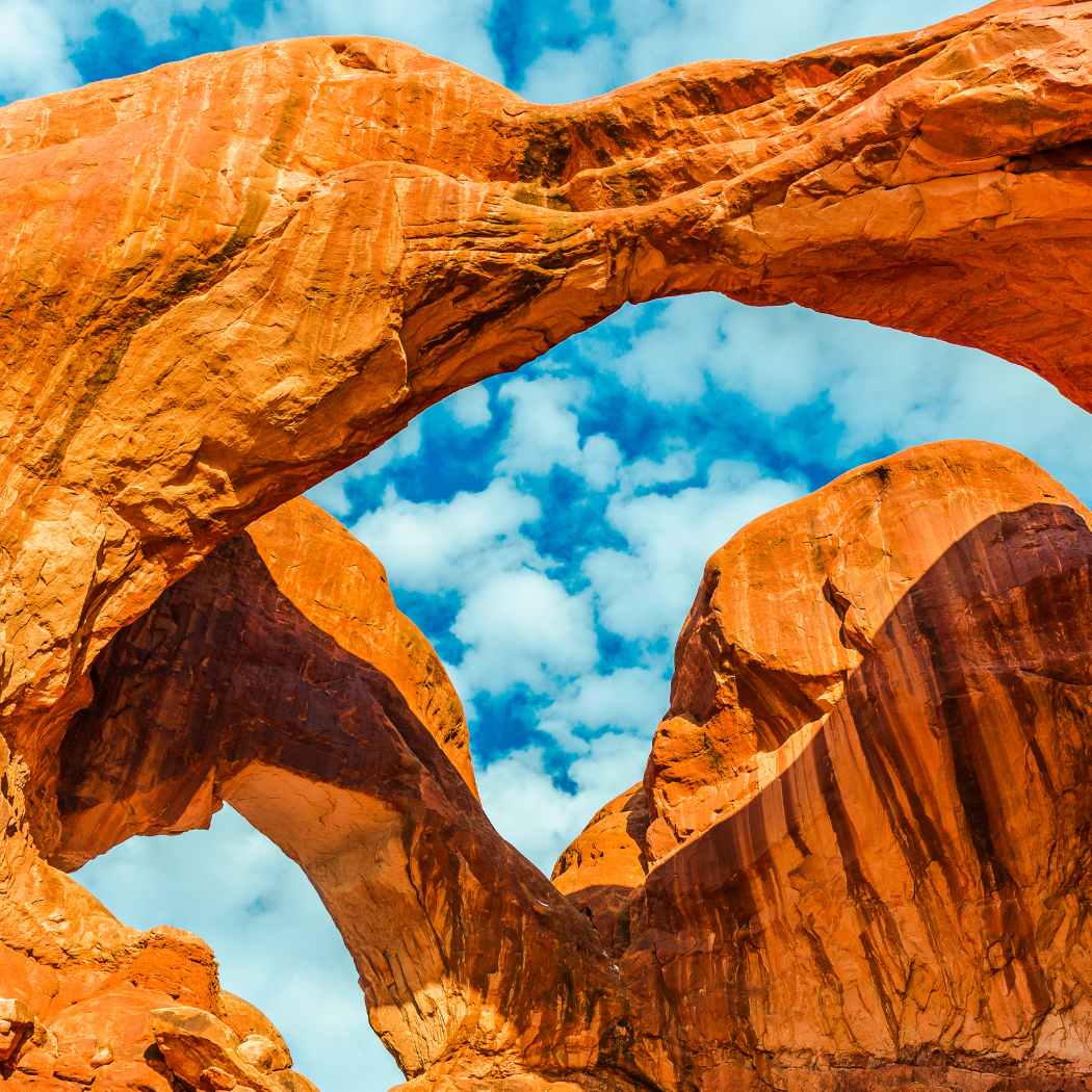 Natural red rock arch formations against a blue sky with clouds.
