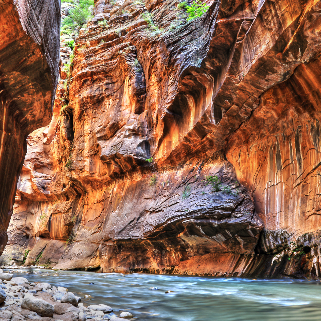 Narrow canyon with steep, red cliffs and a flowing river at the bottom.