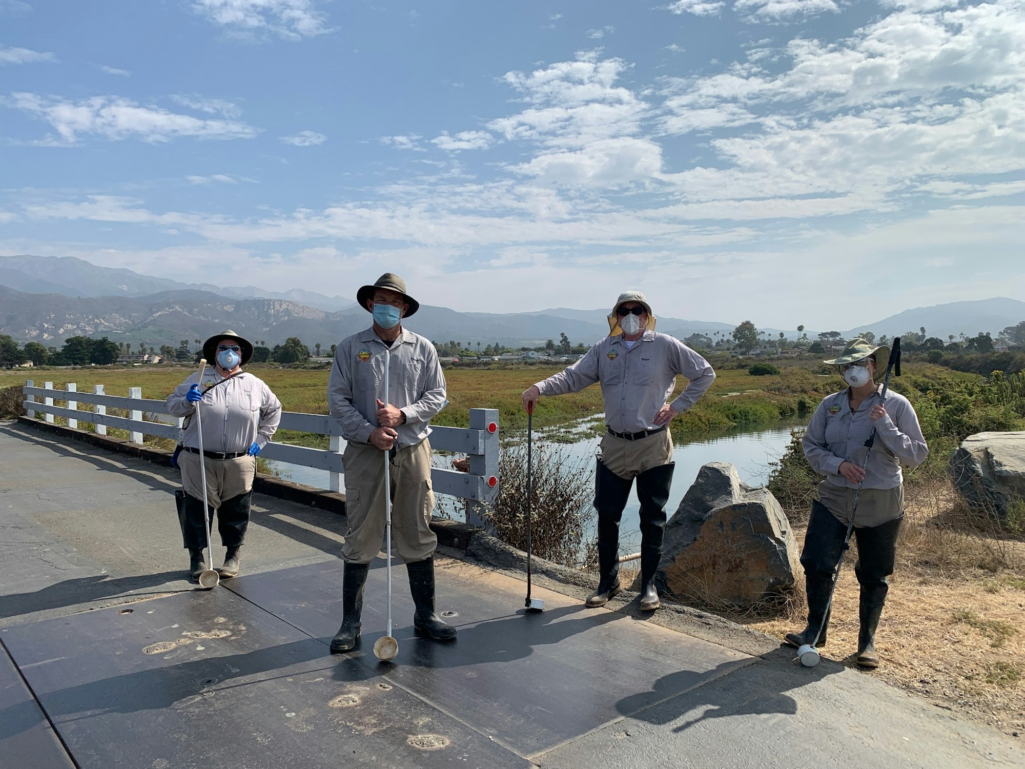 Vector control staff posing next to a bridge crossing over a channel at the saltmarsh.