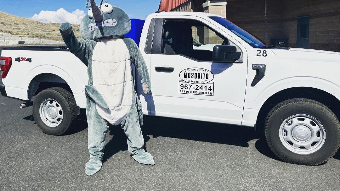 Person in mosquito costume next to a mosquito control district truck.