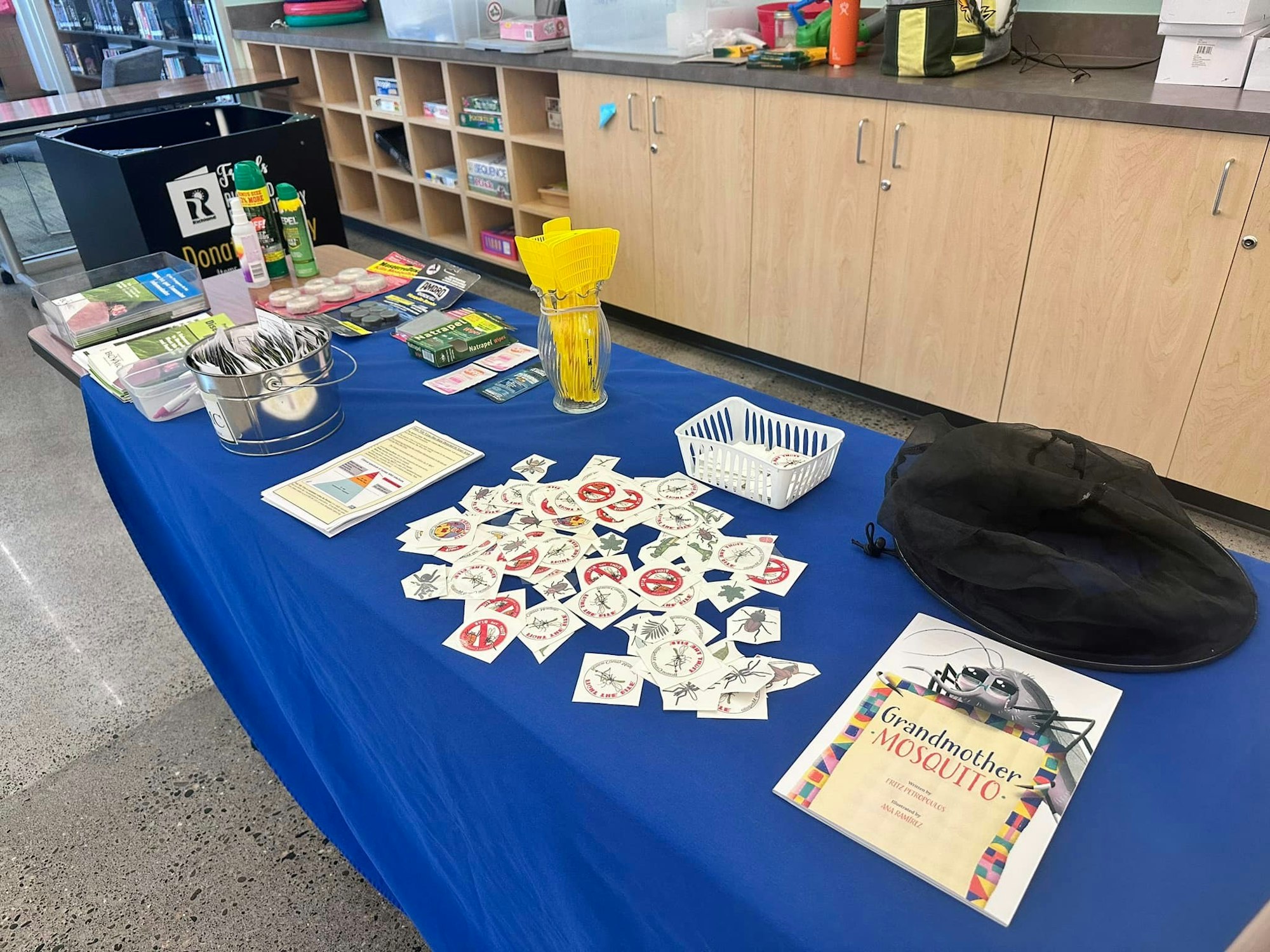 A table with educational materials, stickers, insect repellent, and a mosquito trap setup display.