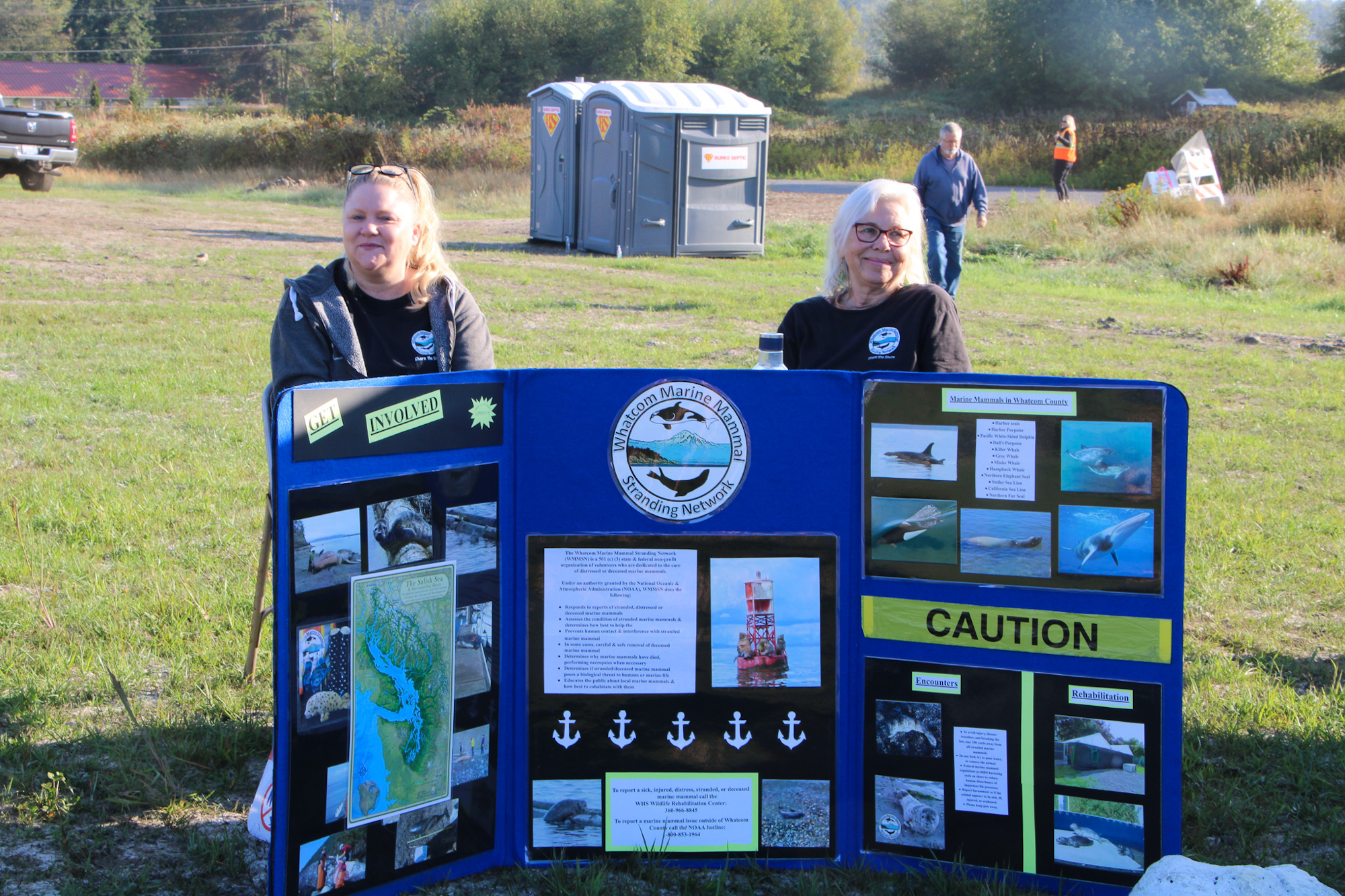 Two people at an outdoor event with a display for the Whatcom Marine Mammal Stranding Network.