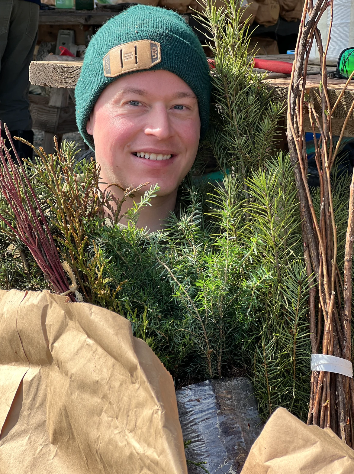 A person in a green beanie surrounded by various plants and branches.