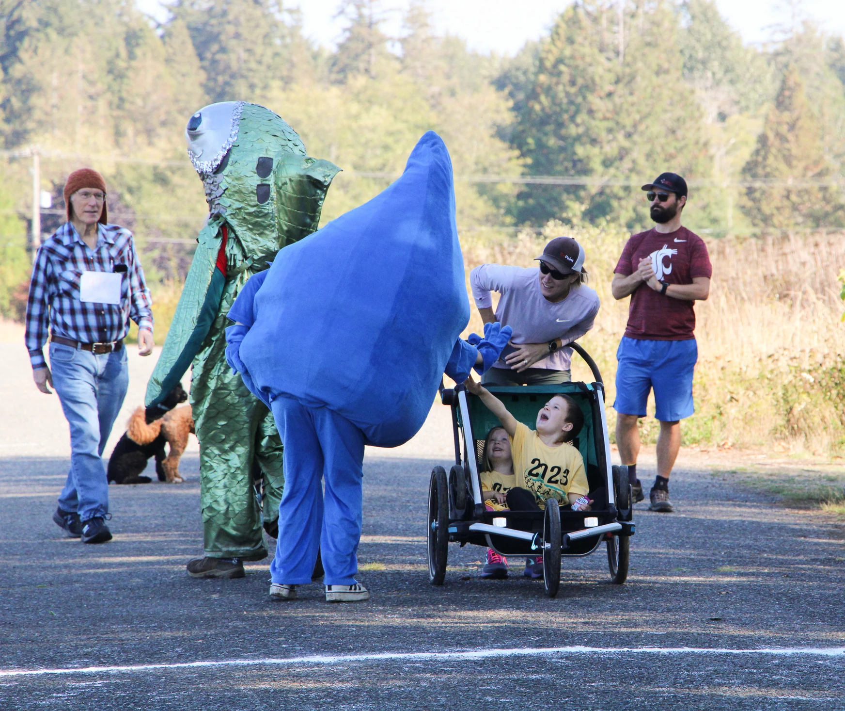 People in costumes interacting with children in a stroller during an outdoor event.