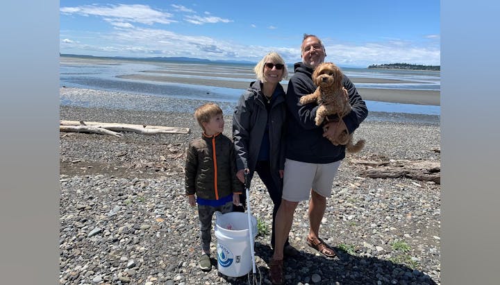 Three people and a dog on a rocky beach, holding a bucket with a scenic coast in the background.