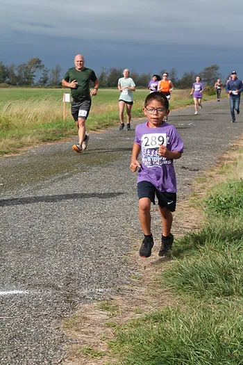 A group of people, including a child with a race number, are running on a rural road.