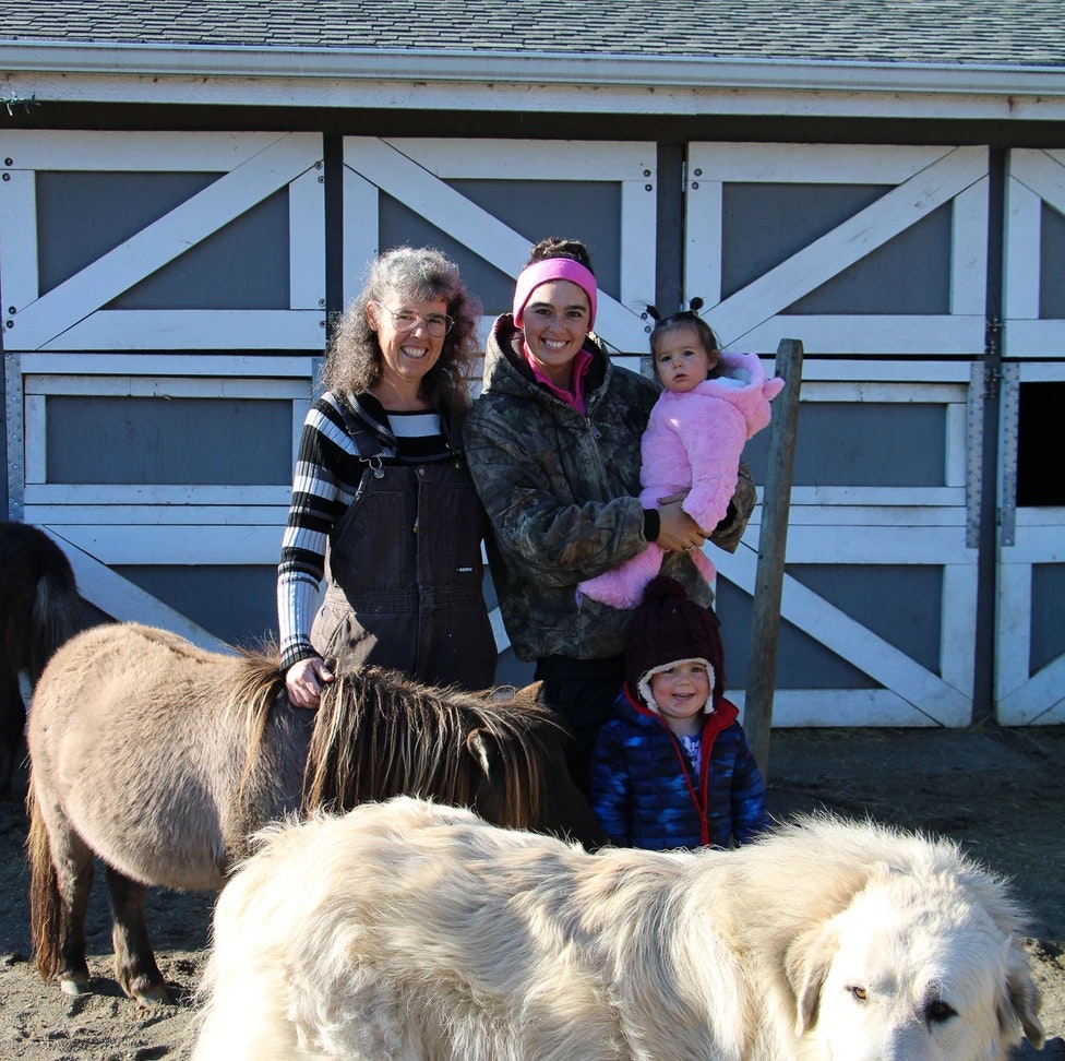 A group of people with two small children, a dog, and a pony in front of a barn.