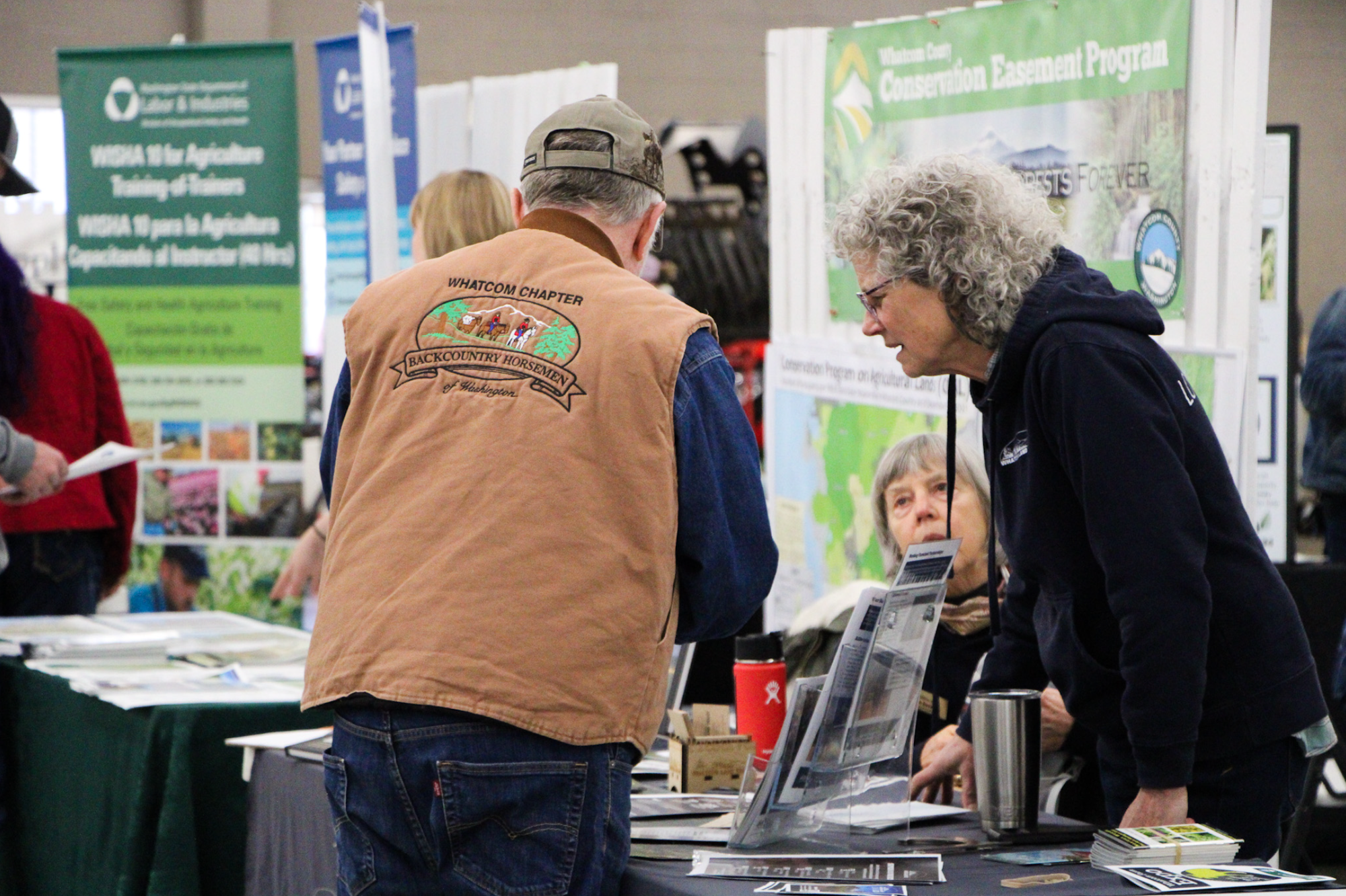 People interacting at a conservation program booth, with brochures and informational displays.