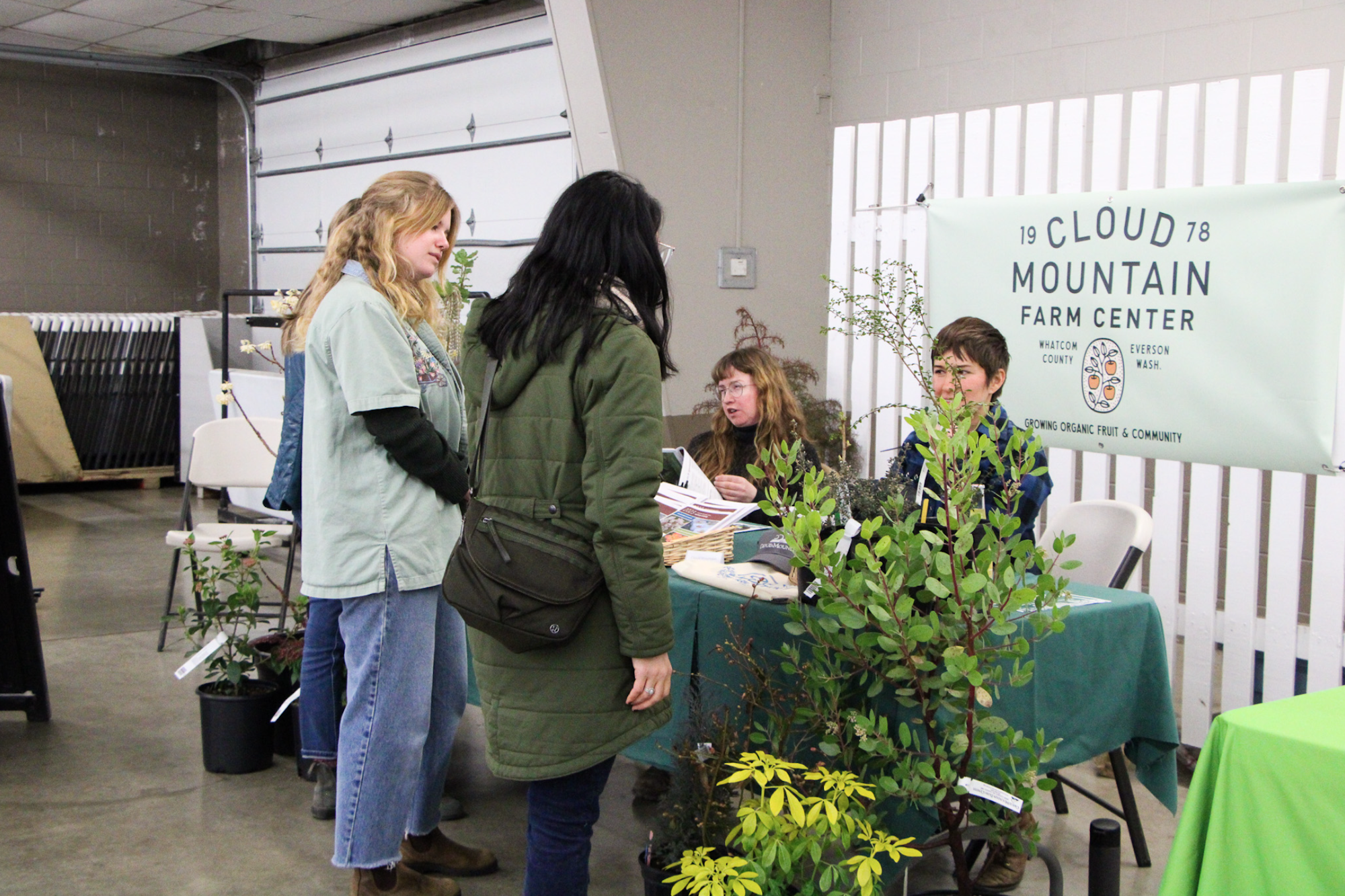 People at a booth for Cloud Mountain Farm Center, displaying plants and materials.