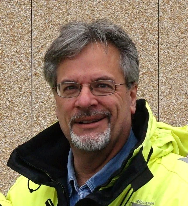 A person with glasses and a goatee wearing a jacket, smiling at the camera.