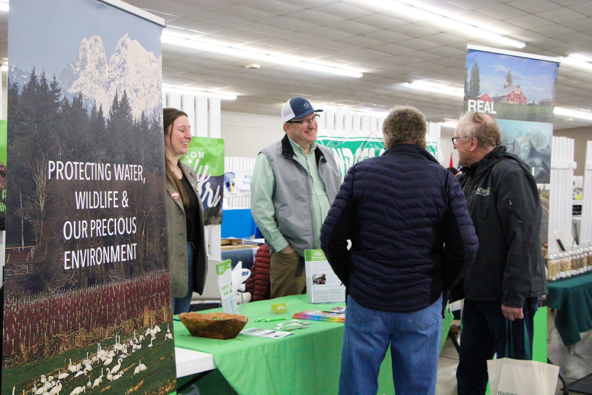 A group of people interacting at a booth with a banner about protecting the environment.