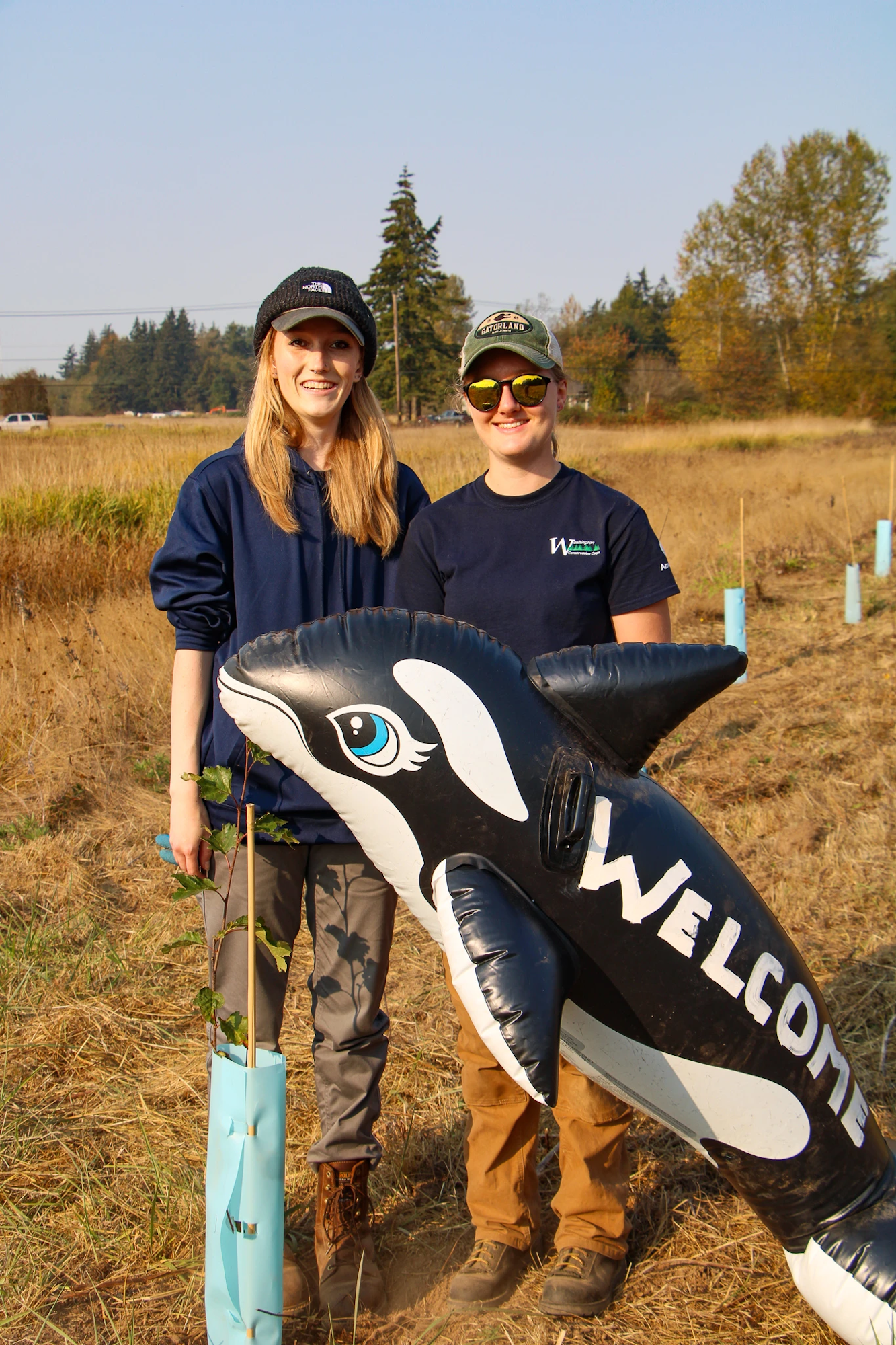 Two people outdoors with a large inflatable killer whale that says "Welcome."