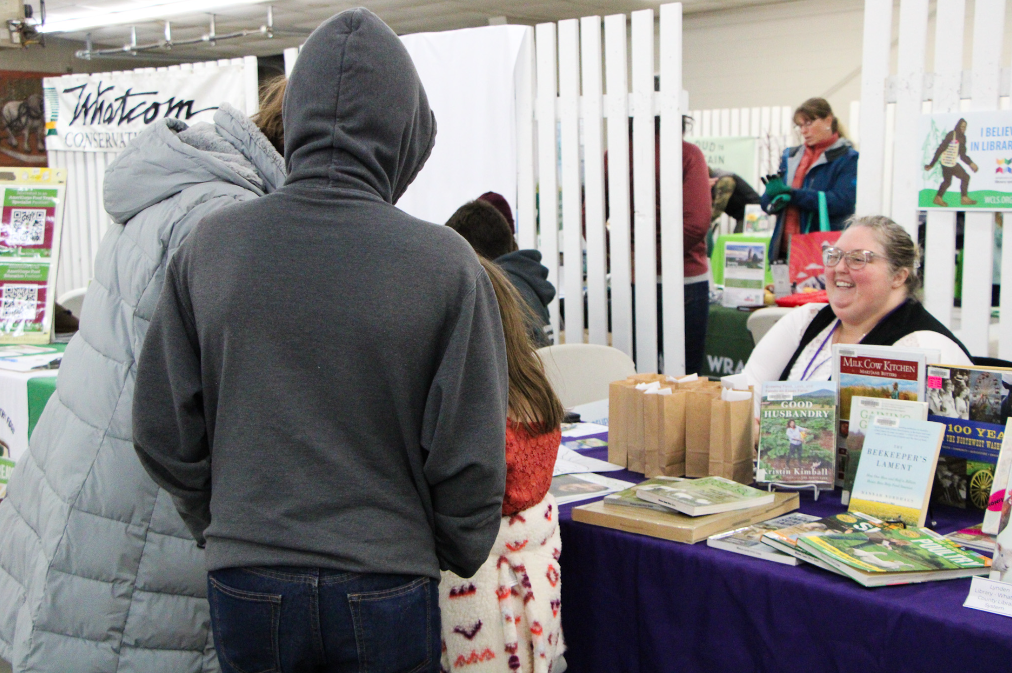 People at a booth with books and pamphlets, one person sitting and smiling.