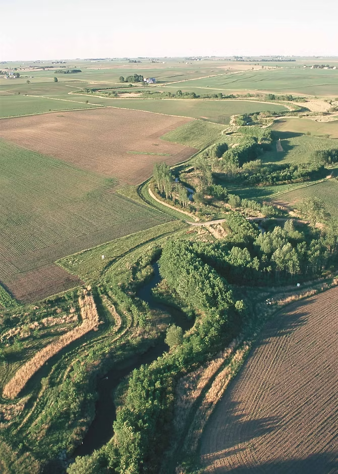 Aerial view of a rural landscape with fields, a winding river, and patches of trees.