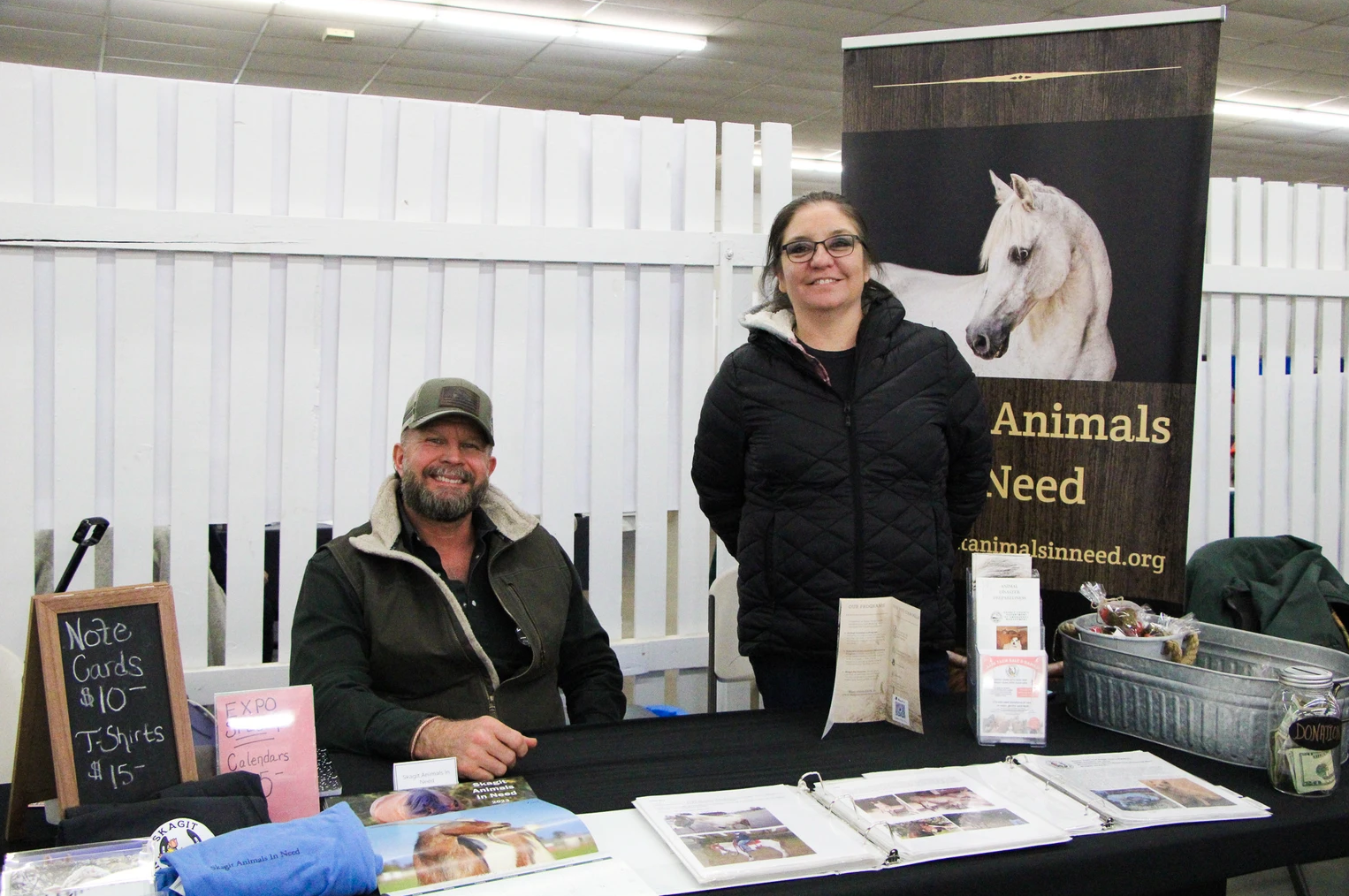 Two people at a booth for an animal charity, with note cards and T-shirts for sale.