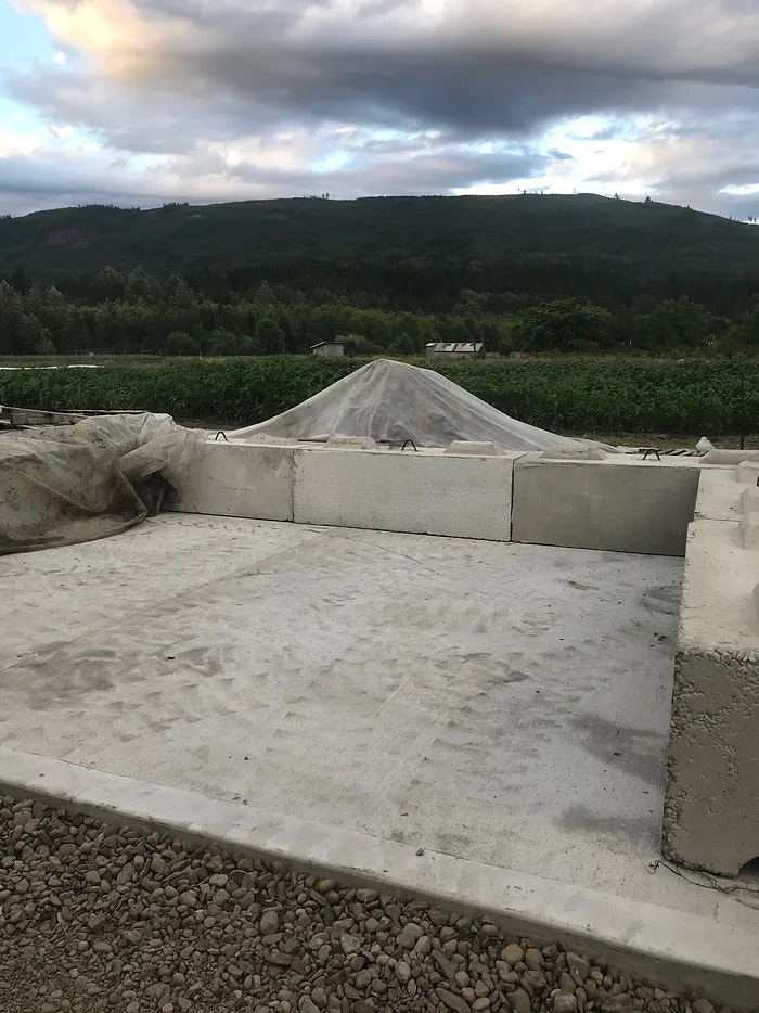 Concrete blocks surround a flat area, with a rock pile covered by a tarp in the background, set against a rural landscape.