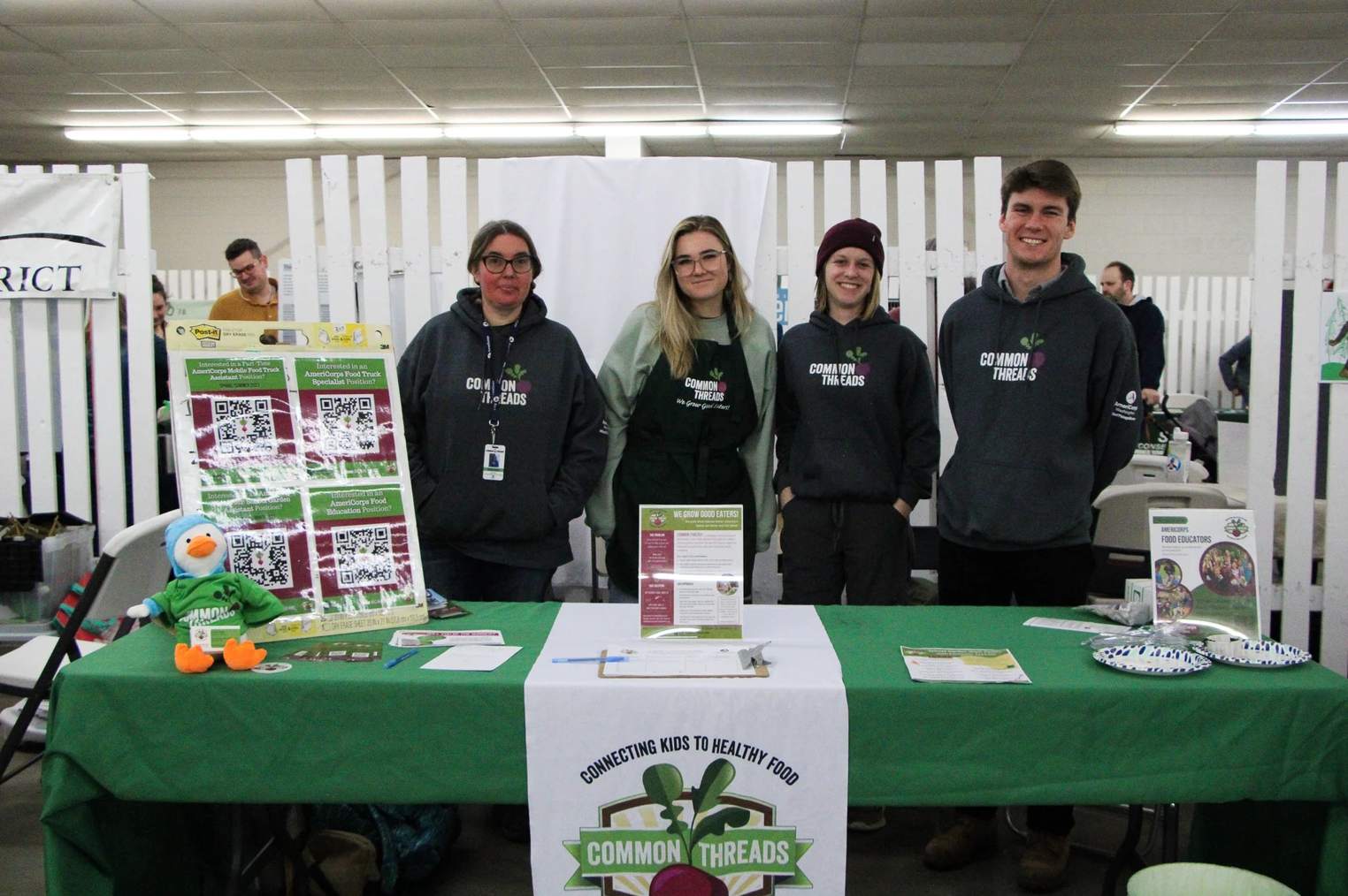 Four people at a "Common Threads" booth, promoting healthy food education with displays and pamphlets.