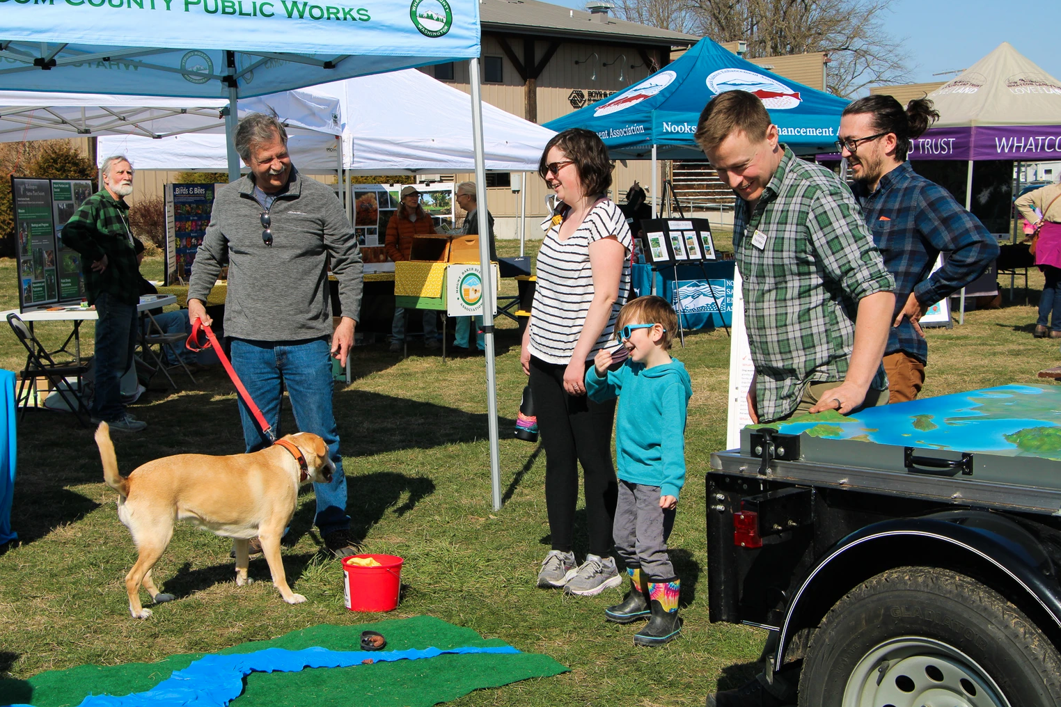 People at an outdoor event with a dog, tents, and informational displays.