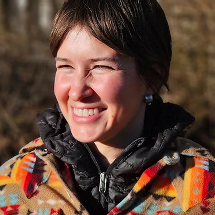 A person smiling outdoors, wearing a colorful patterned jacket.