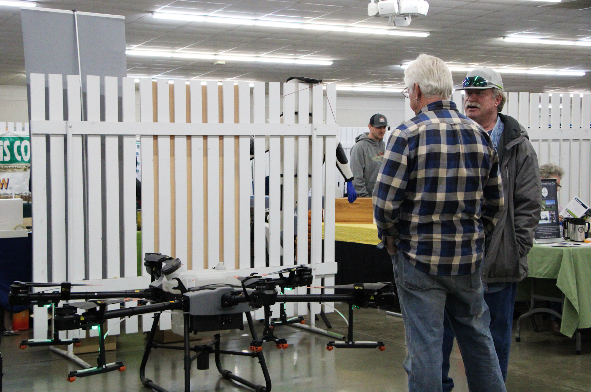 Two men talking at an indoor exhibition with a large drone on the floor nearby.