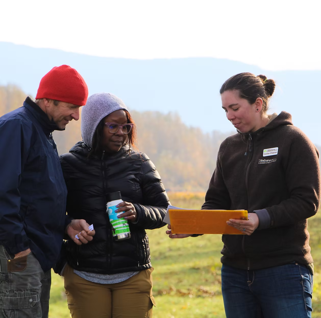 Three people outdoors, one holding paperwork, possibly discussing or reviewing something.