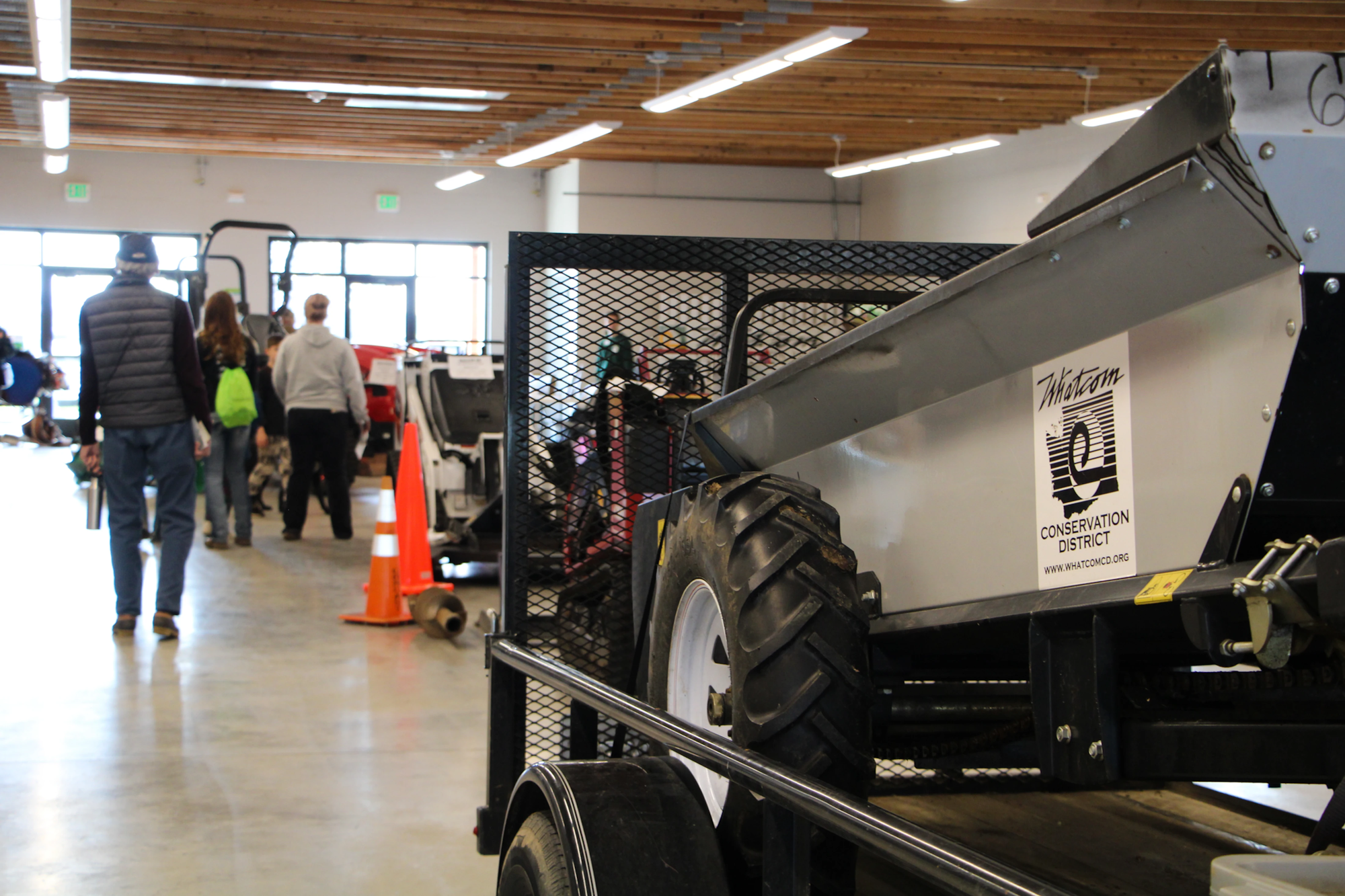 Indoor farming equipment display with people walking, featuring a Whatcom Conservation District sticker.