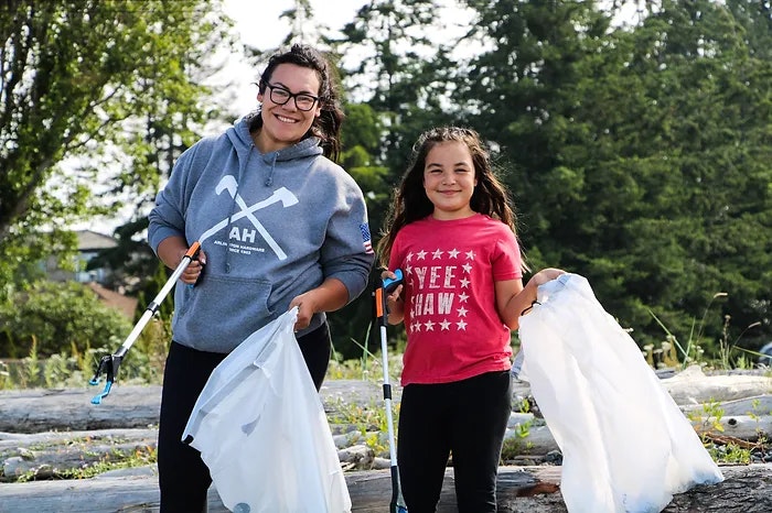 Two people holding trash bags and grabbers, cleaning up outdoors.