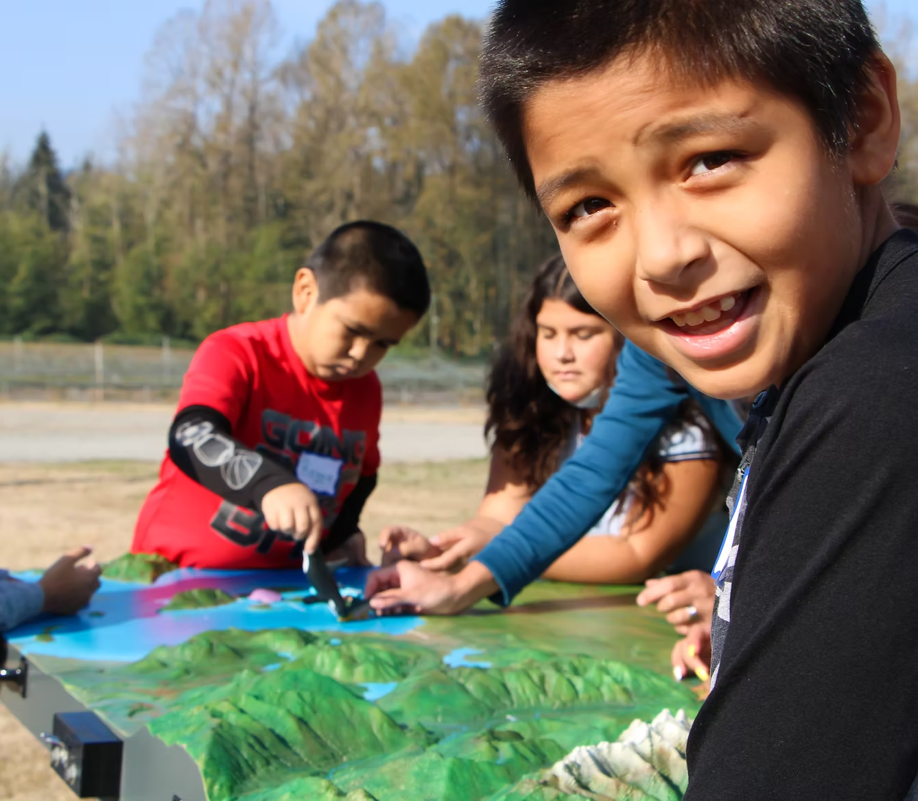 Children interacting with a 3D landscape map outdoors.