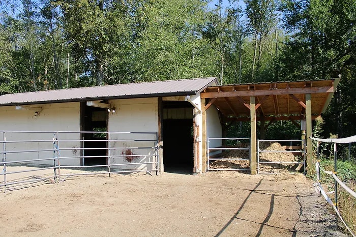 A stable or barn with open gates, surrounded by trees.