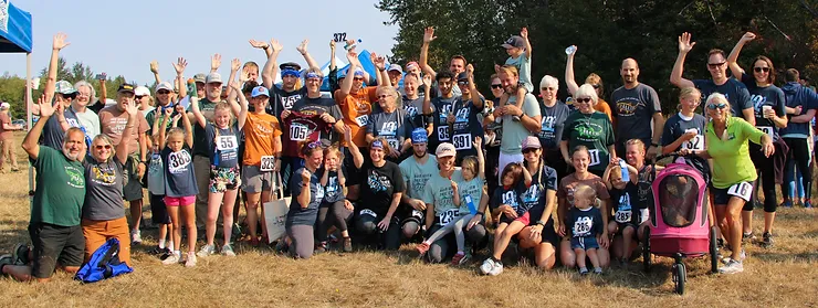 A group of people outdoors, some wearing race numbers, celebrating with arms raised.