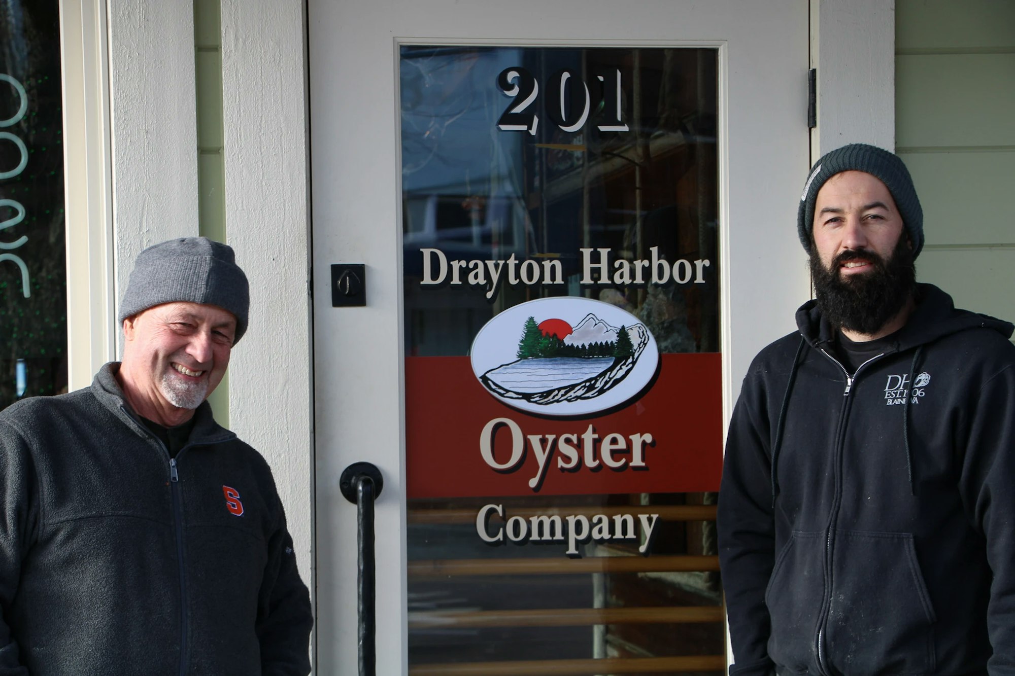 Two people standing by a door with the sign "Drayton Harbor Oyster Company."