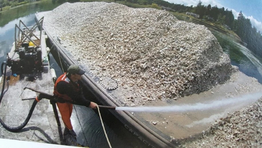 Person power-washing a barge loaded with shells on a river.