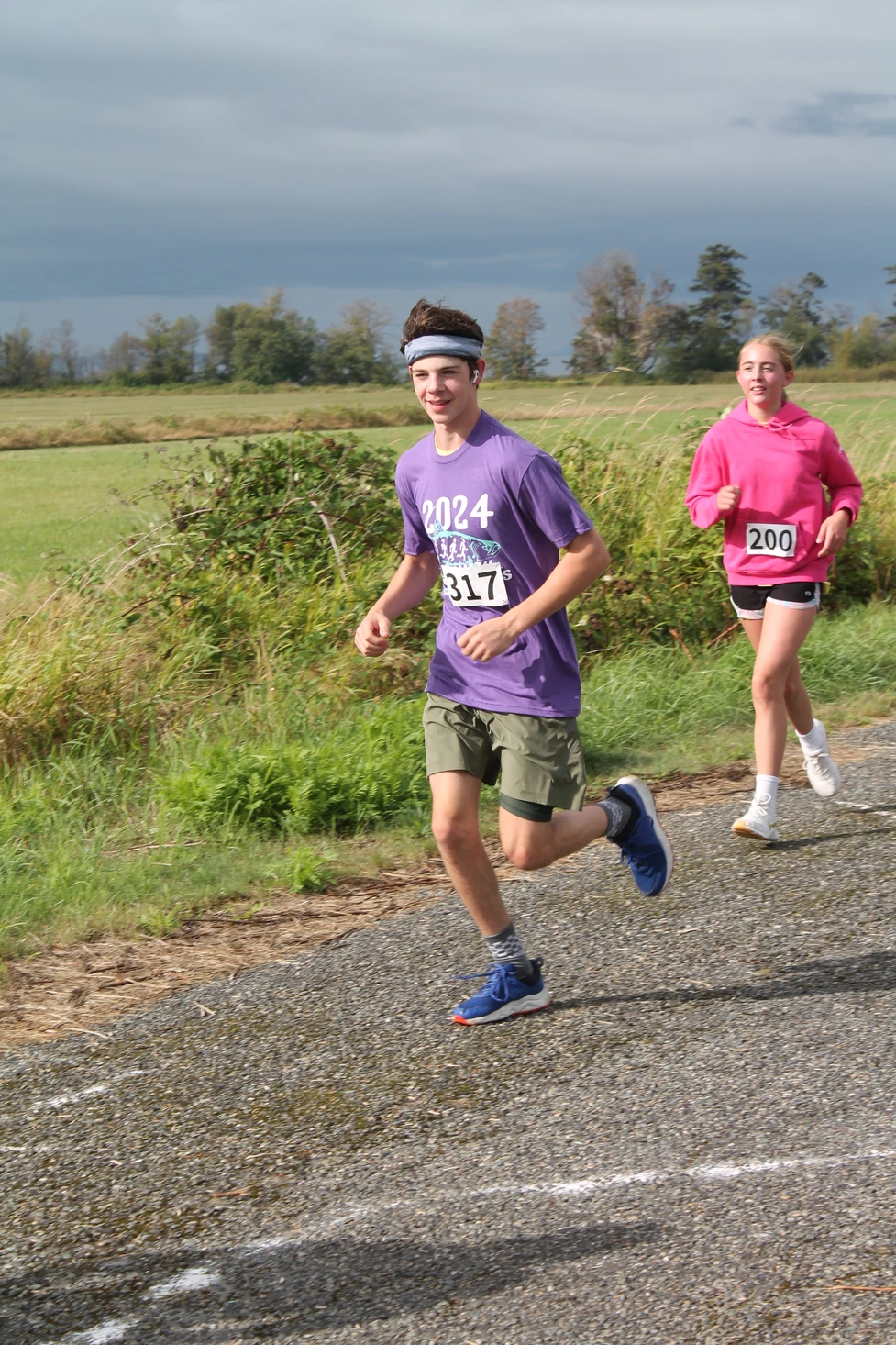 Two people running outdoors with race bibs, one in purple and one in pink, on a rural path.