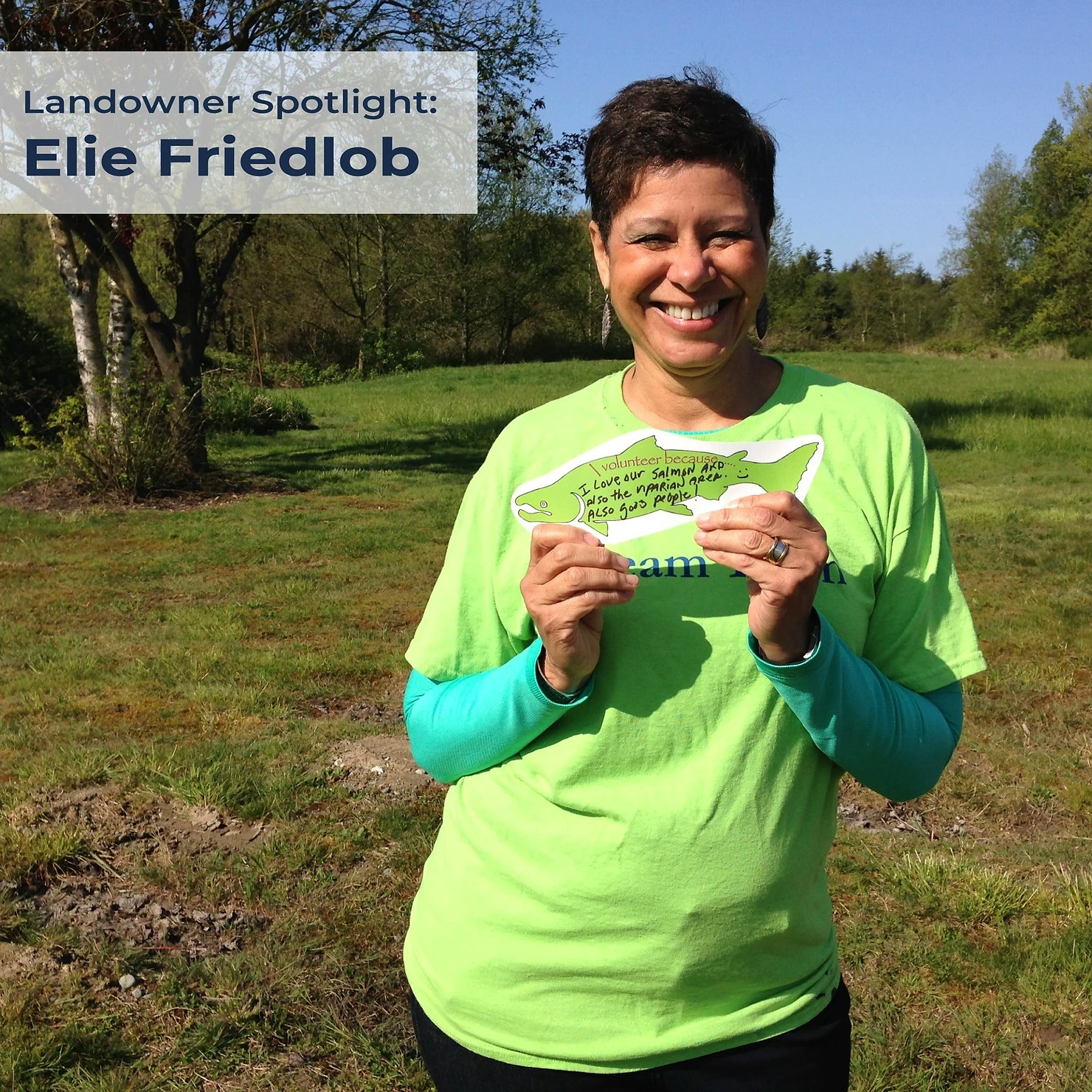 A smiling person in green holds a handwritten sign about volunteering, outdoors. Text reads "Landowner Spotlight: Elie Friedlob".