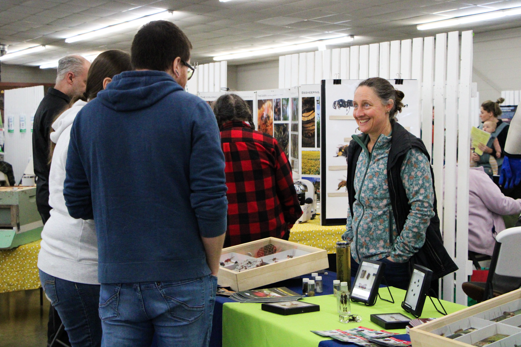 People interacting at a booth in a convention or expo setting, with displays and informational materials on the table.