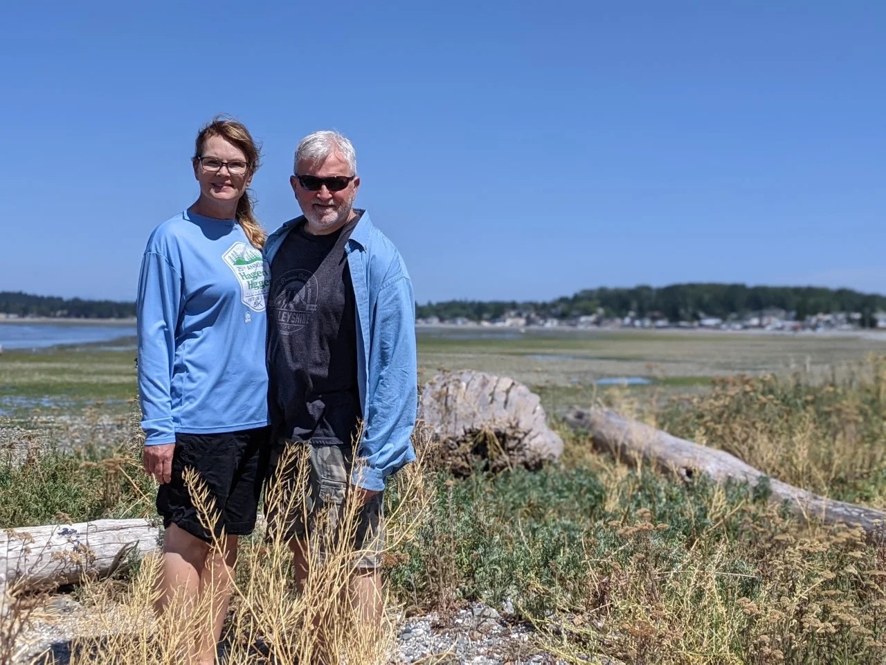 Two people standing in a field with dry grass and a distant view of a coastal landscape.