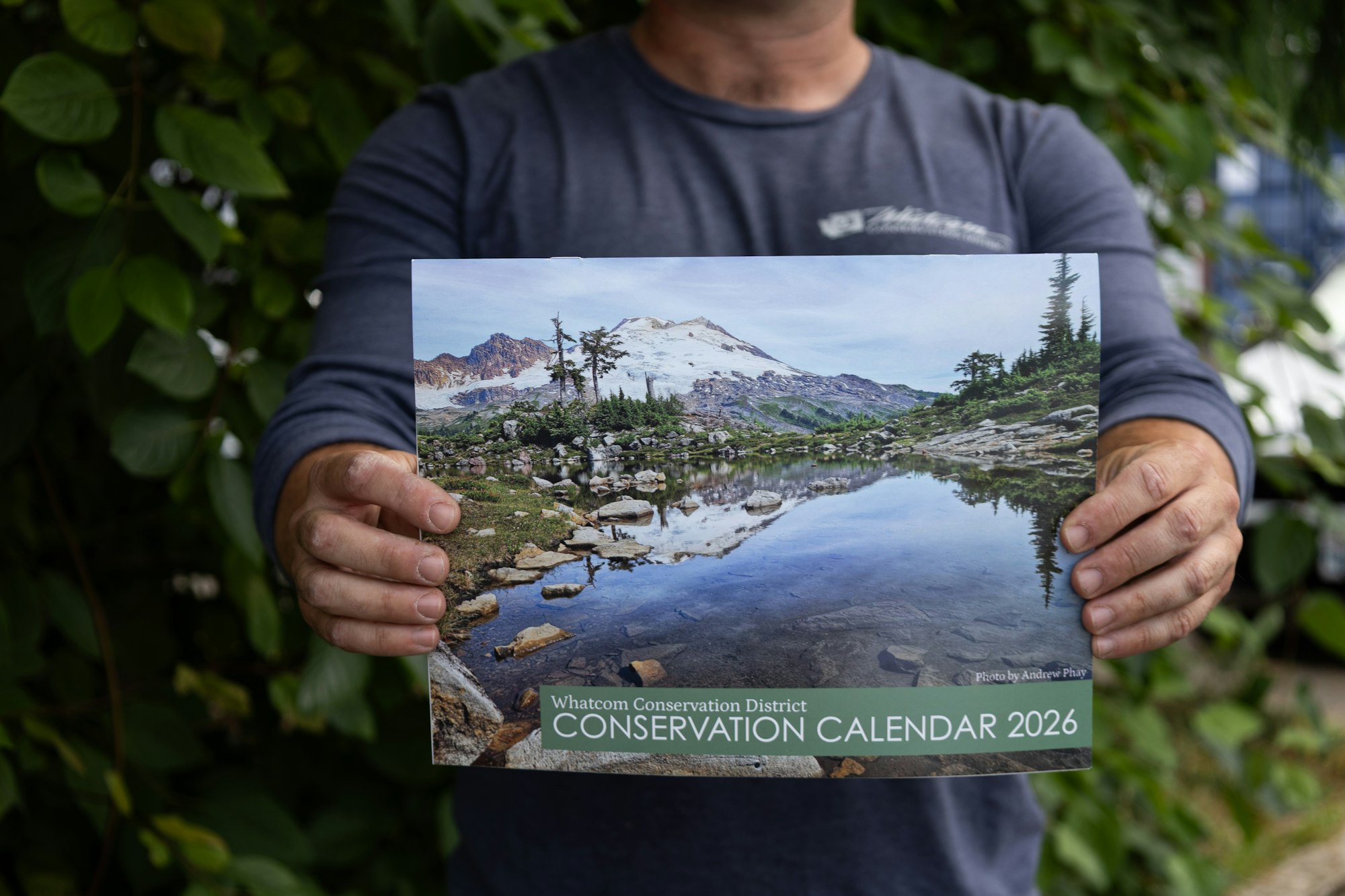 A person holds a calendar featuring a scenic landscape for the Whatcom Conservation District, marked for 2026.