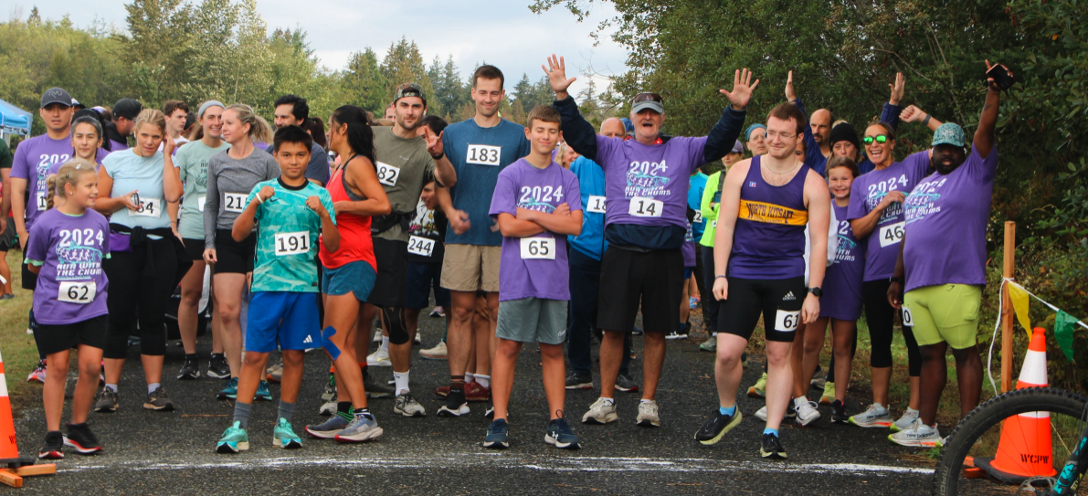 A group of runners of various ages at the starting line of a race, wearing numbered bibs and sporty attire.