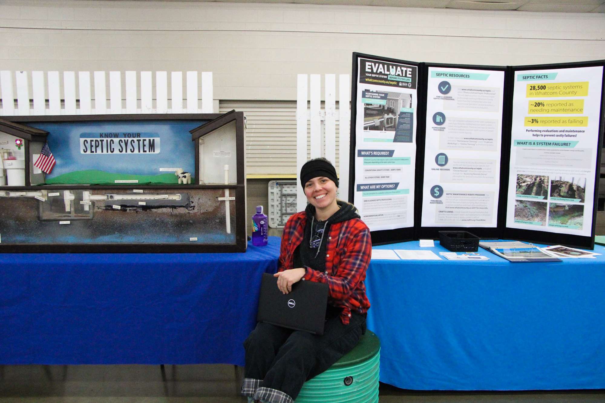 A person sitting next to a "Know Your Septic System" display and informational booth.