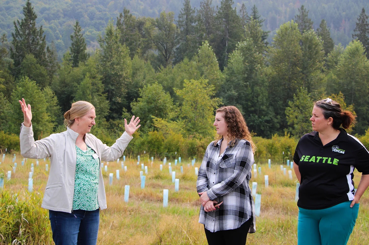 Three people talking in a field with trees and plants around them.