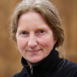 A person with light hair is wearing a dark jacket, set against a plain background.