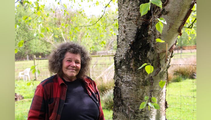 A person smiling next to a tree with fresh green leaves, outdoors.