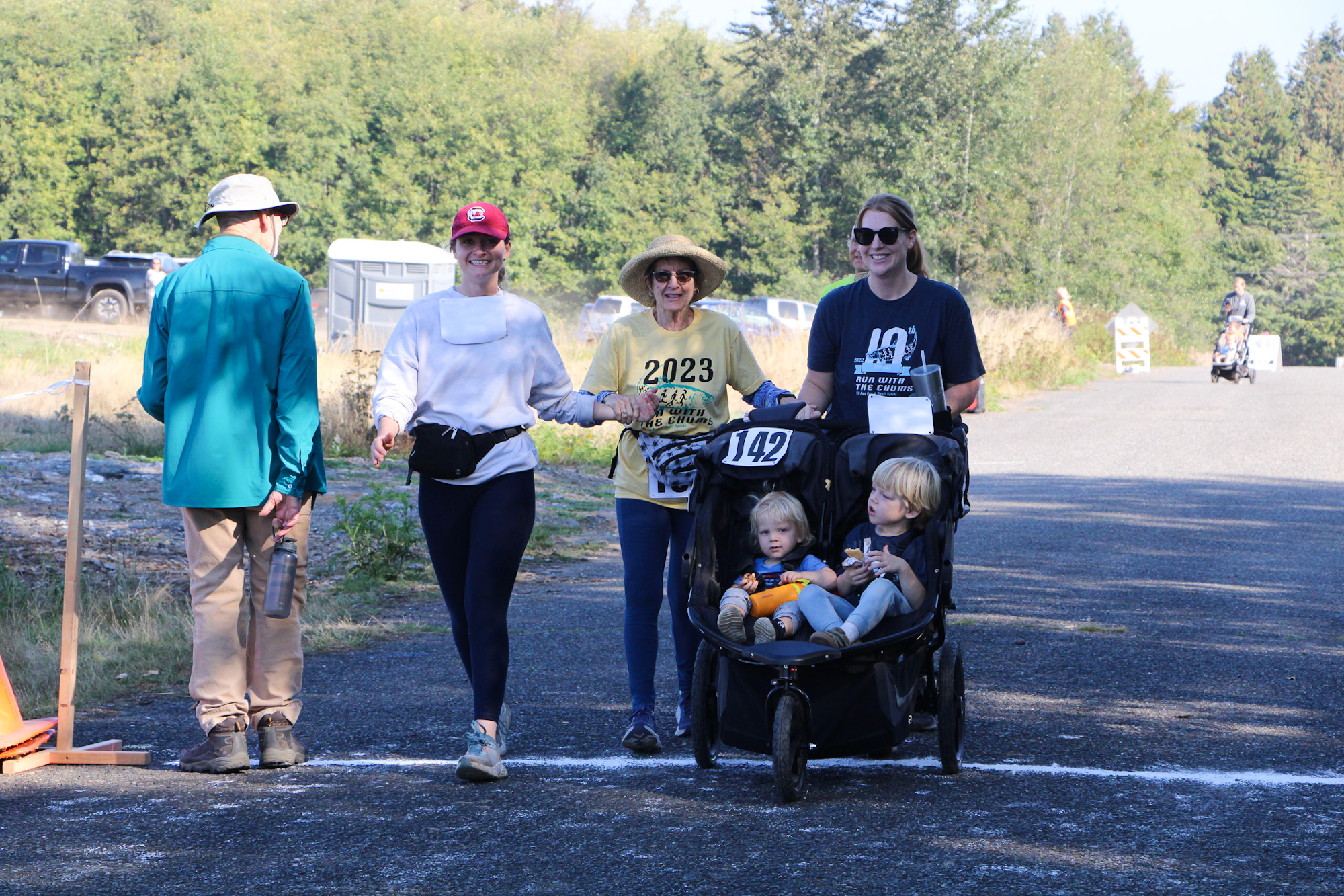 People walking, one pushing a stroller with two kids, in a park or outdoor area. They're near a finish line.