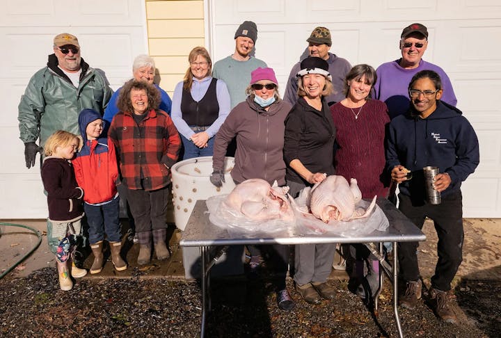 Group of people smiling outdoors with two raw turkeys on a table.