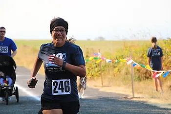 A woman is running a race wearing bib number 246. There are other participants and a dog in the background.